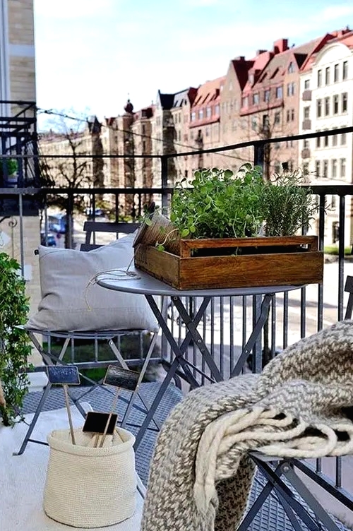 a cozy Scandi balcony, a rug, pillows, throws, potted plants and tiny coffee tables for winter