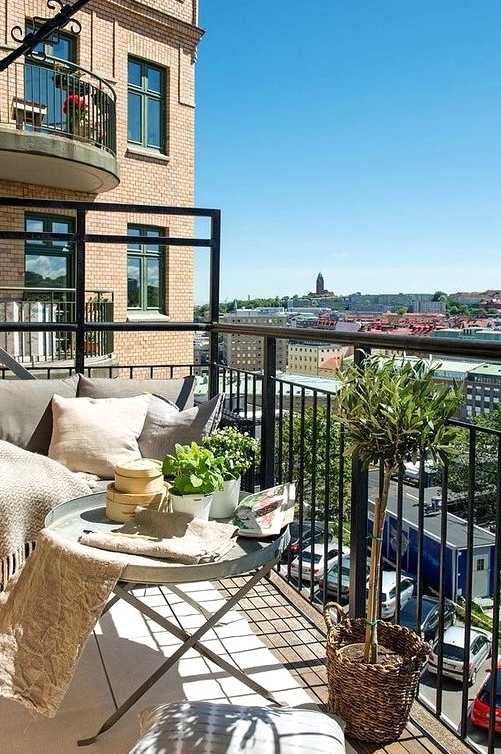 a neutral balcony with metal furniture, neutral textiles, potted greenery and lots of pillows is very welcoming