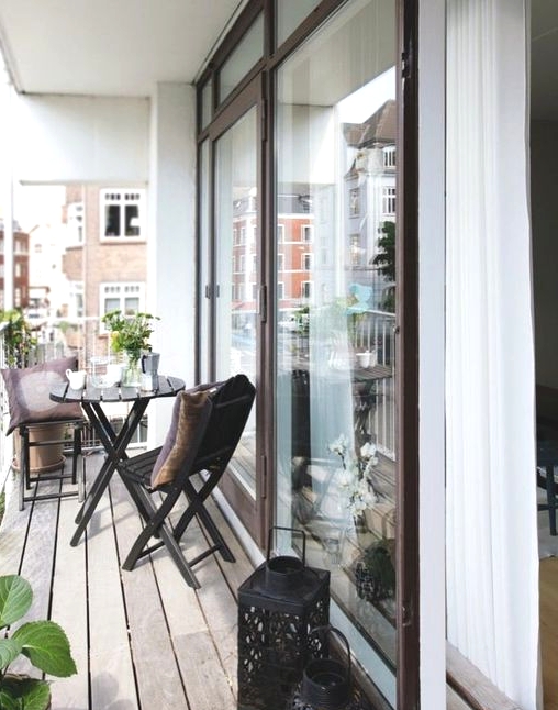 a Scandinavian balcony with black folding chairs and a table, black candle lanterns, potted greenery and blooms