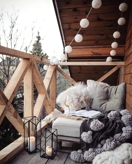 candle lanterns, lights garlands, a seat with fluffy pillows and tassel blanket for a Scandinavian balcony or terrace look
