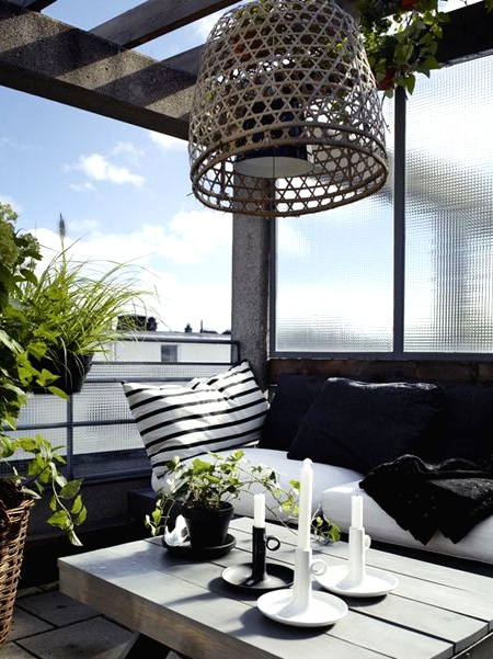 a stylish Nordic balcony with a black bench and black and white textiles, a wooden coffee table, a woven pendant lamp and some potted greenery