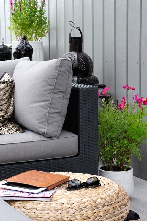 a Nordic balcony with grey and black furniture and grey upholstery, jute poufs, potted greenery and blooms and candle lanterns in Moroccan style