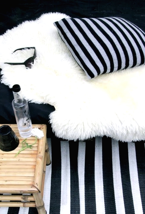 a Scandinavian balcony with a black and white striped rug and a pillow, faux fur and a stained side table