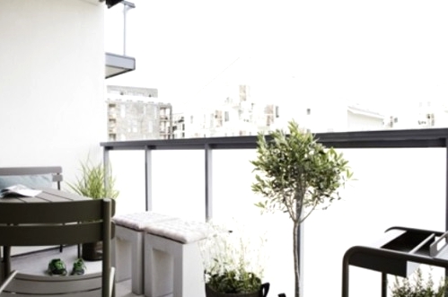 a monochromatic Nordic balcony with black and grey metal and wood furniture, white cinder stools, potted greenery and plants is welcoming