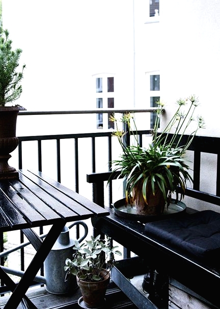 a Nordic balcony in black, with simple wooden furniture, potted greenery and blooms is a stylish idea for those who love moody colors
