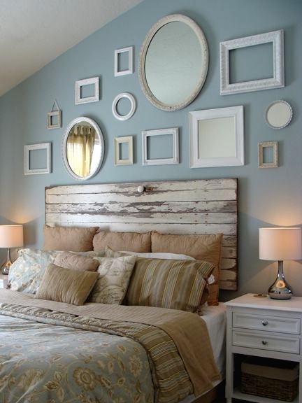 a vintage bedroom with a blue accent wall, a gallery wall of empty frames, a bed with a shabby whitewashed headboard, white nightstands and printed bedding