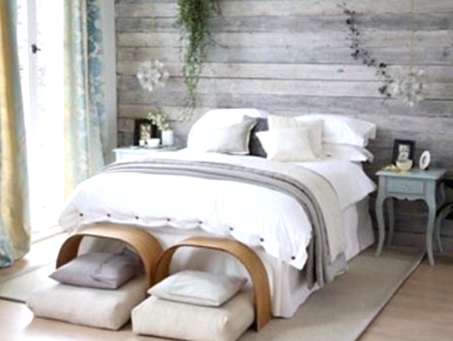 an airy bedroom with a shabby chic whitewashed headboard, a bed with neutral bedding, a couple of benches and pillows, vintage nightstands