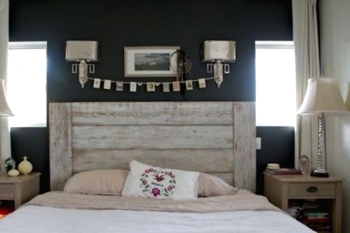 a farmhouse bedroom with black walls, a bed with a whitewashed headboard, neutral nightstands and table lamps, sconces and artwork