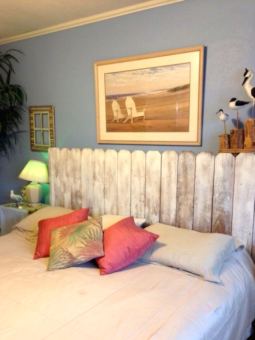 a bedroom with blue walls, a bed with a whitewashed headboard, artwork and a potted statement plant is cool