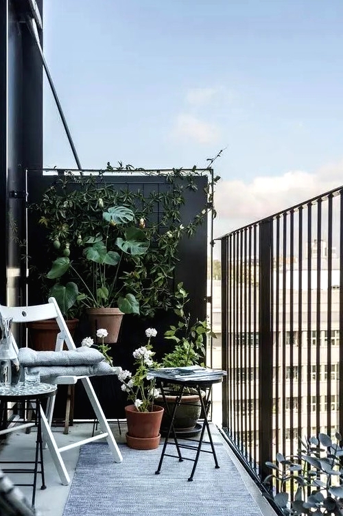 a black balcony done with a couple of folding chairs and a small coffee table plus a lot of greenery around