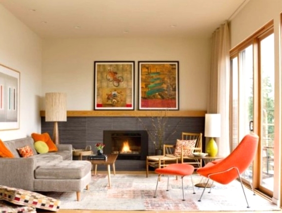 a colorful mid-century modern living room with a built-in fireplace, a grey sectional, a fiery red chair, a wooden chair, a low table and colroful artworks