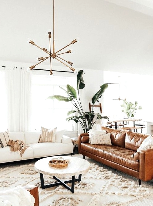 a light-filled mid-century modern living room with a creamy and amber leather sofa, a round table, a boho rug and a chic chandelier