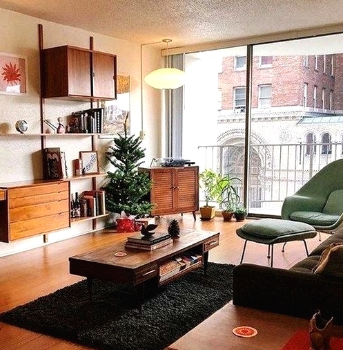 a lovely mid-century modern living room with a green chair and a footrest, a black sofa, chic rich stained wooden furniture and potted plants