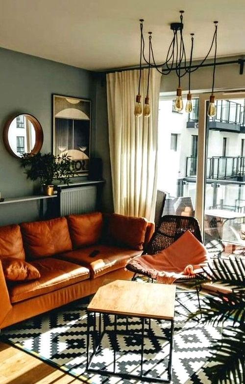 a mid-century modern living room with grey walls, an amber leather sofa, a black woven chair, an open shelf with decor and mirrors