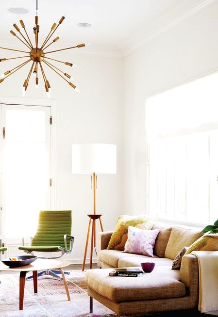 a mid-century modern living room with a bold printed rug, a sectional sofa with bright pillows, green chairs and a coffee table, a burst chandelier