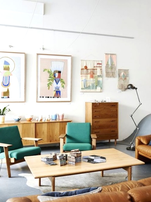 a bright mid-century modern living room with stained furniture, green chairs, an amber leather sofa, a low coffee table, a gallery wall and beautiful potted plants