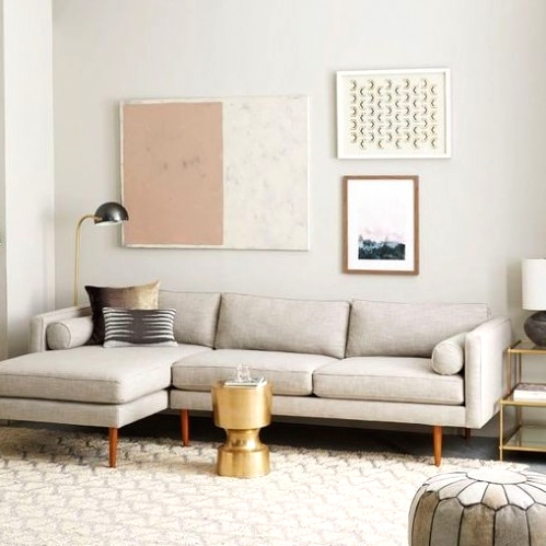 a neutral mid-century modern living room with a grey sectional, a neutral rug, a grey pouf, a gold side table and a lovely gallery wall
