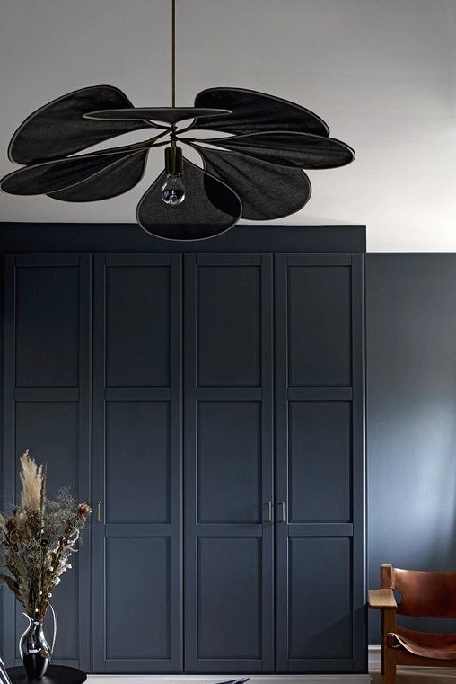 a moody bedroom with graphite grey walls and a graphite grey wardrobe with paneling, a black petal pendant lamp and a bed with a navy and white bedding