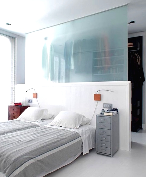 a neutral bedroom with a half wall and a frosted glass wall that divides the bedroom and walk-in closet in the space