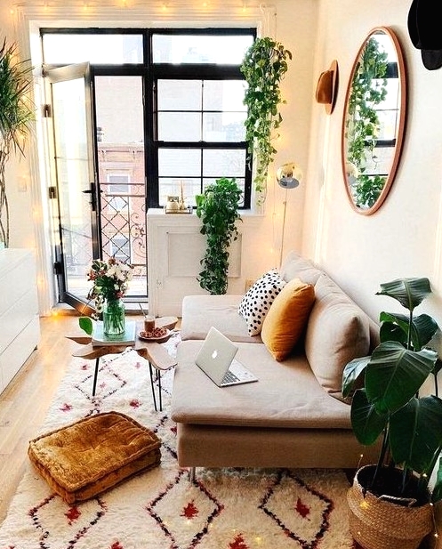 a tiny boho living room with a small neutral sofa, a white storage unit, geo printed rug, lights and potted greenery