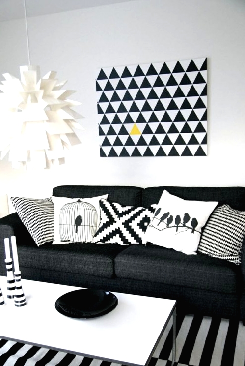 a black and white living room with a black sofa, a striped rug, a white coffee table, a geometric artwork and a wihte paper pendant lamp plus geometric pillows