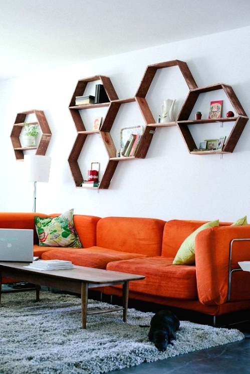 a living room with an orange sectional sofa, a stained hexagon shelf on the wall, a grey rug and a stained coffee table plus a printed pillow is cool
