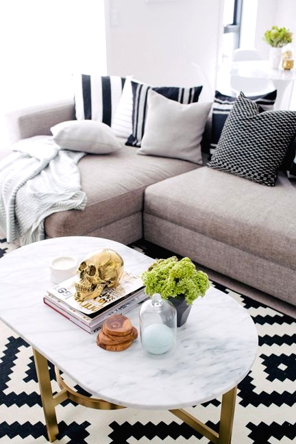 a Scandinavian sitting space with a grey sofa, neutral and striped pillows, a geometric black and white chair, an oval table with pretty decor