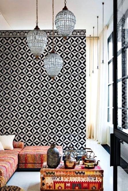 a bold Moroccan living room with a black and white geometric tile wall, a low Moroccan sofa and a bright coffee table, pendant lamps and gold side tables