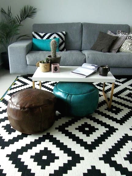 a stylish modern living room with a grey sofa, geometric and bright pillows, geo printed rug and leather poufs plus a potted plant