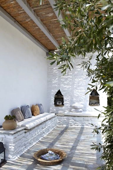 a lovely Mediterranean patio with a built-in bench and striped pillows, Moroccan lanterns, a tray with a magazine and greenery around