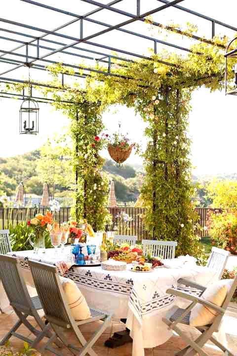 a pretty and livly Mediterranean terrace with a large table, grey chairs, greenery and blooms around and a lovely view