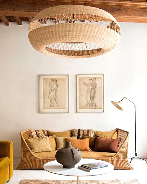 a chic living room with a wicker bench with lots of pillows, a mustard chair, a jute rug and a round table, a wicker pendant lamp