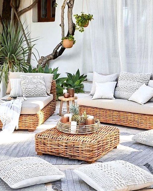a coastal outdoor space with wicker outdoor furniture and a side table, neutral teixtiles and lots of plants around