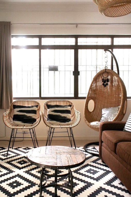 a modern living room with a brown sofa, a round table with a wooden tabletop, wicker chairs, a wicker pendant chair is amazing