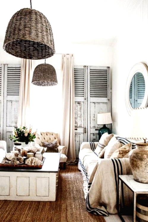 a shabby chic coastal living room with neutral furniture, a low coffee table with a black tabletop, shabby chic shutters, wicker pendant lamps, striped furniture covers