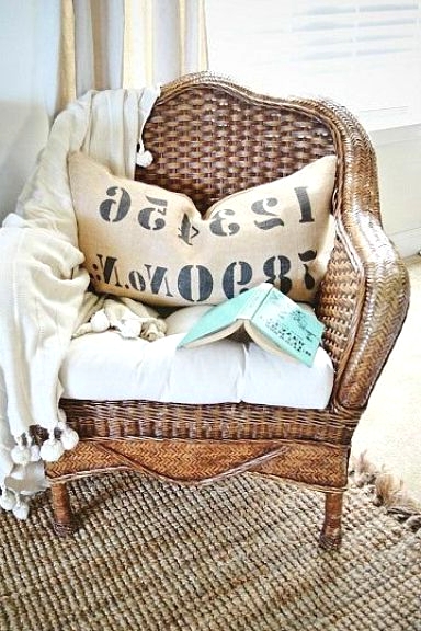 a wicker chair with neutral upholstery, a printed pillow and a neutral blanket is a lovely solution for comfortable reading