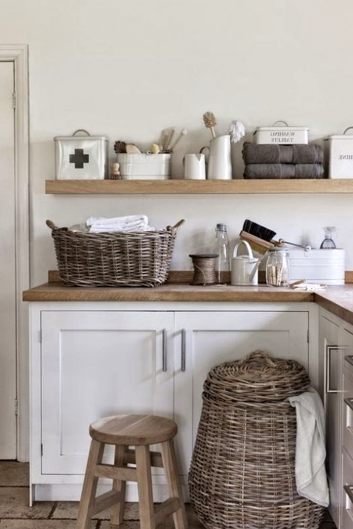 a modern rustic laundry room with white cabinets and stained shelves, baskets for storage and a wooden stool is a lovely space to be