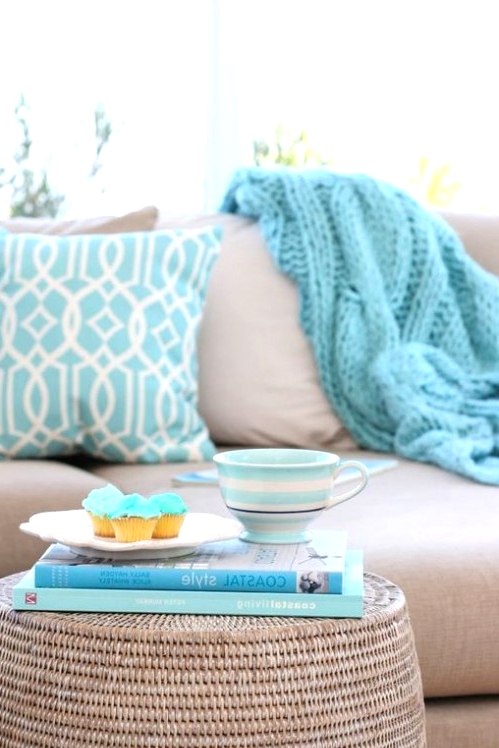 a dove grey sofa with blue printed pillows, a white wicker coffee table with blue books are great for a coastal space