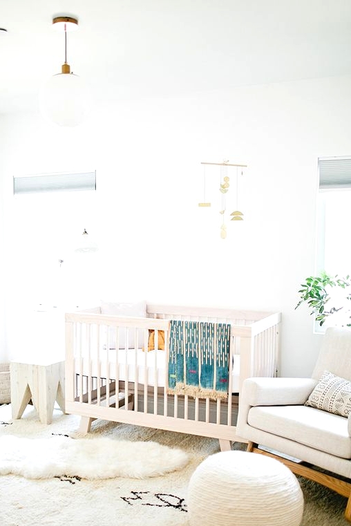 a neutral mid-century modern meets boho nursery with a white crib, a creamy rocker chair, a round pouf, a white stool, layered rugs