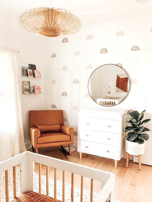 an earthy tone mid-century modern nursery with pretty wallpaper, a white dresser, an amber leather chair, a white crib, a wooden pendant lamp and books