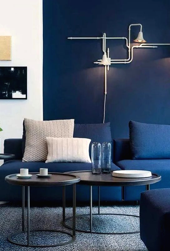 a bright modern living room with navy walls, navy sofas, black side tables and cool art, unique industrial-inspired sconces