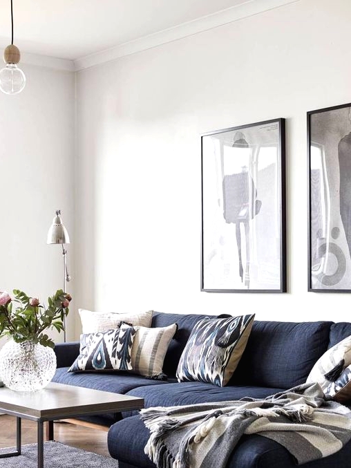 a Scandinavian living room with a navy sectional sofa, a coffee table, black and white artwork and a floor lamp plus some blooms