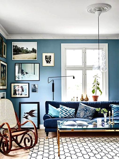 a welcoming living room with dusty blue walls, a creative gallery wall, a navy sofa, a glass coffee table and a rocker chair