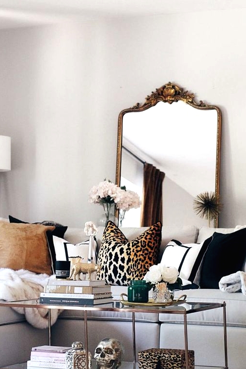 a chic neutral living room with a white sectional, printed pillows including a leopard print one, a glass coffee table with a leopard print box