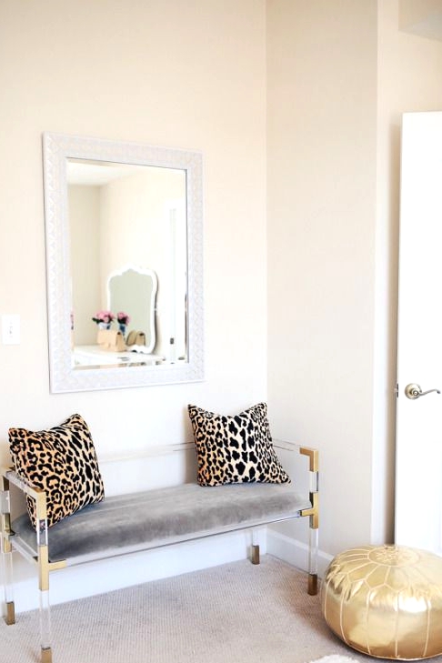 a glam entryway with an acrylic bench with leopard print pillows, a shiny gold pouf and simple layered rugs is stylish and lively