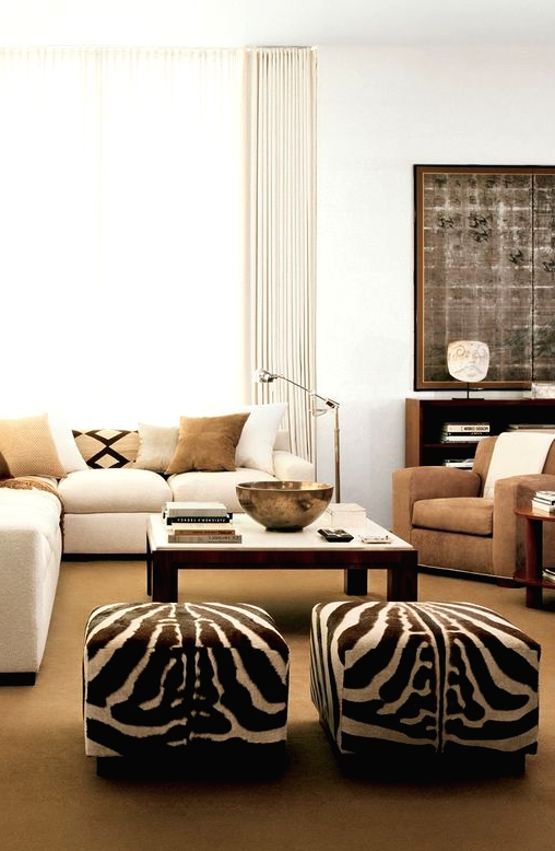 a modern living room with a creamy sectional with earthy pillows, a taupe chair, a large coffee table and zebra print poufs is cool