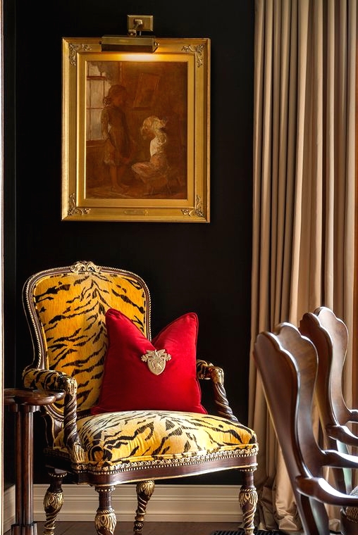 a refined vintage space with black walls, a yellow and black zebra print chair with a red pillow, an artwork and a vintage wardrobe with cane