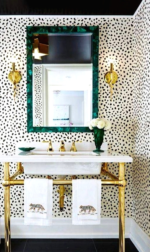 a stylish bathroom with Dolmatin print walls, a free-standing sink on gold legs, a mirror in a green frame and gold sconces is wow