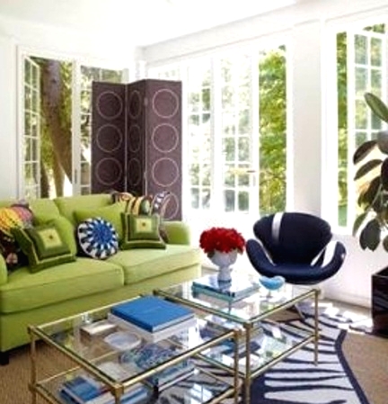a colorful living room wiht white walls, a green sofa, layered rugs including a faux zebra rug, glass coffee tables and colorful pillows is amazing