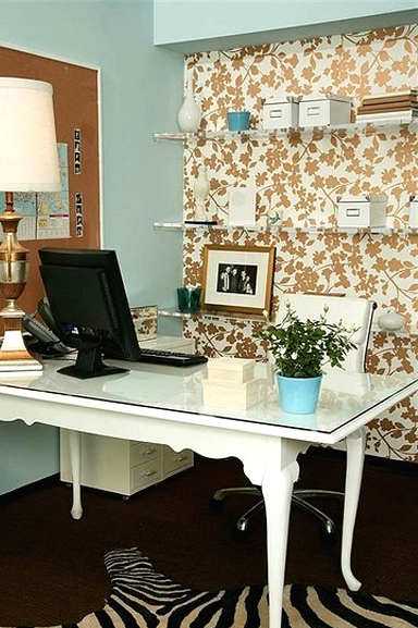 a modern working space with a gold and white botanical accent wall, a white desk and a chair, a zebra print rug and a memo board